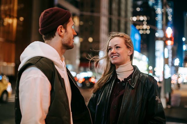 Un uomo e una donna si guardano per strada mentre lei sorride con aria sognante.