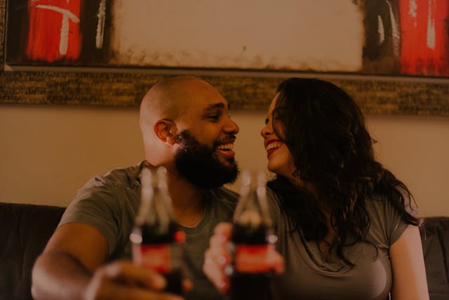 Due ex siedono vicini con una bottiglia di cola e ridono ricordando momenti vissuti insieme.