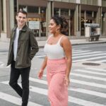 Un uomo e una donna giovani camminano sorridendo su un attraversamento pedonale mentre lui la guarda.