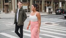 Un uomo e una donna giovani camminano sorridendo su un attraversamento pedonale mentre lui la guarda.