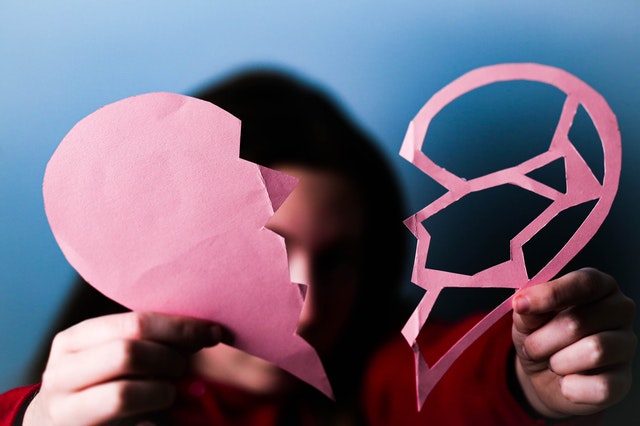 Una persona tiene in mano un cuore di carta spezzato, simbolo di una relazione finita.