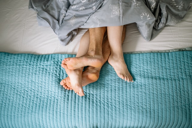 Le gambe di un uomo e una donna sotto un piumone, simbolo dell'infedeltà e della fiducia spezzata nel matrimonio.