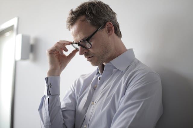 Un uomo con la testa leggermente china tiene gli occhiali in mano e desidera sentirsi compreso.