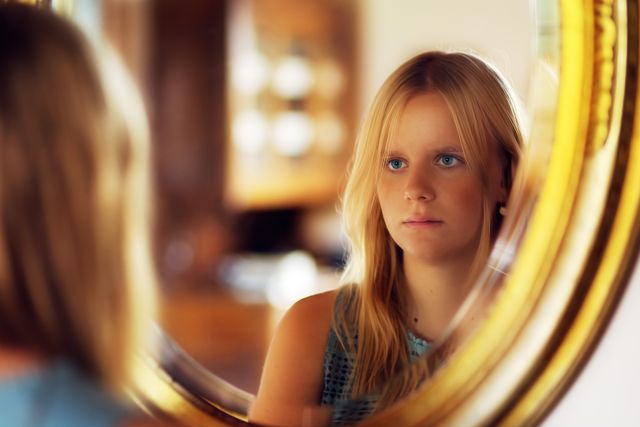 Una donna si guarda seriamente allo specchio, simbolo di una riflessione sincera su ciò che prova.